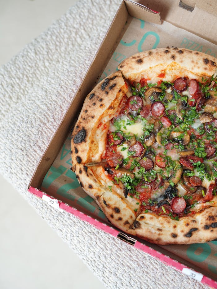 about-us Close-up of a delicious gourmet Italian pizza with fresh toppings in a takeaway box.
