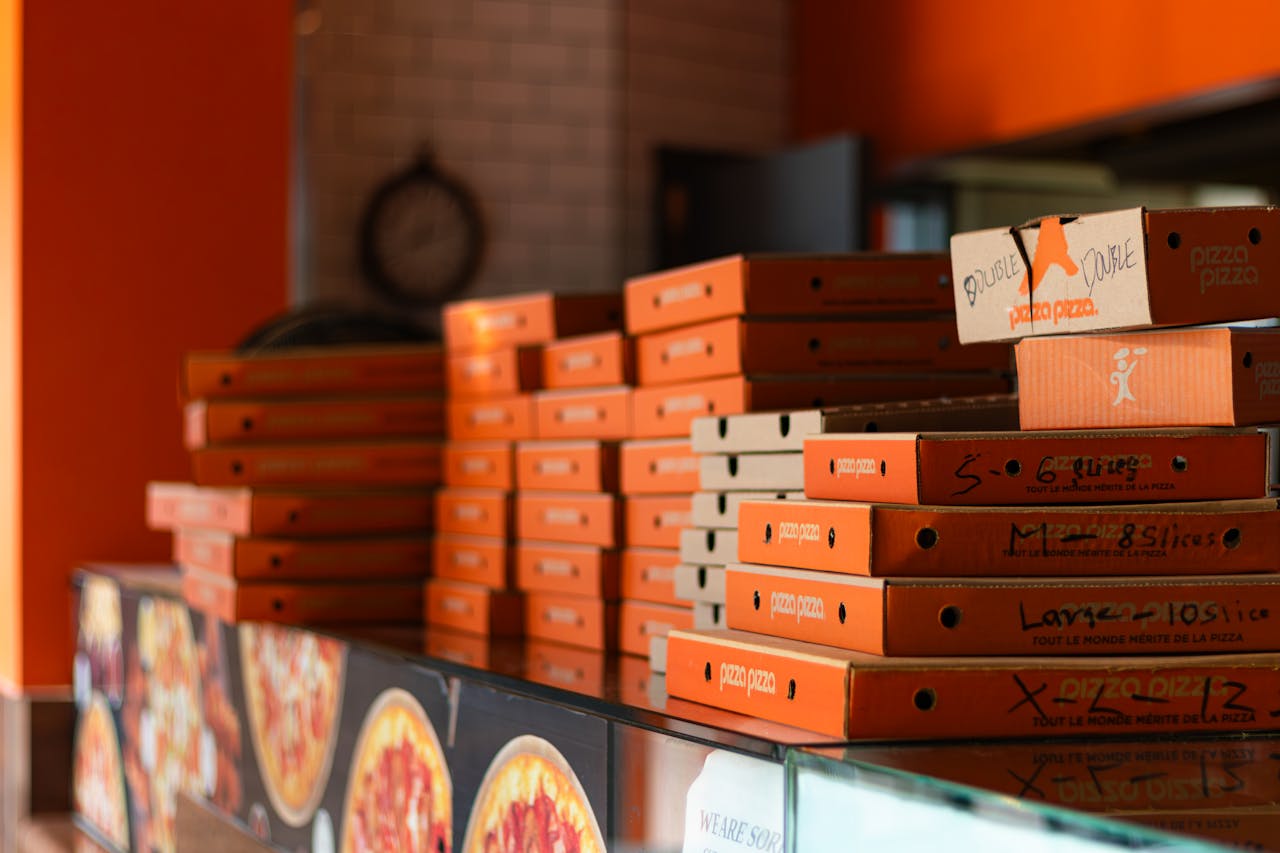 heros-img Stacks of bright orange pizza boxes in a Toronto pizzeria against a warm-toned interior.
